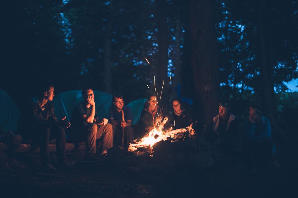 A circle of women gathered around a campfire at night