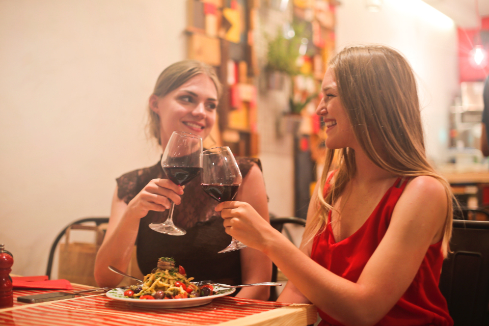 Two women sharing dinner and a toast at a long wooden table
